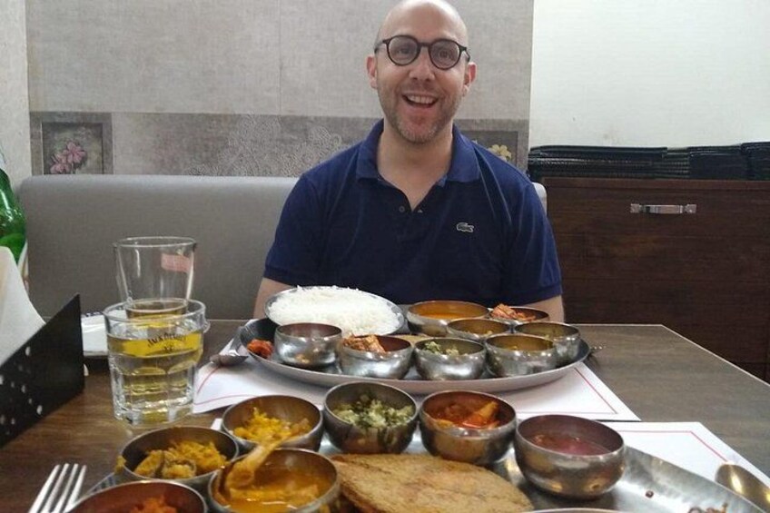 A person seated at a table with various dishes, including rice and multiple bowls of food, in a dining setting. 5