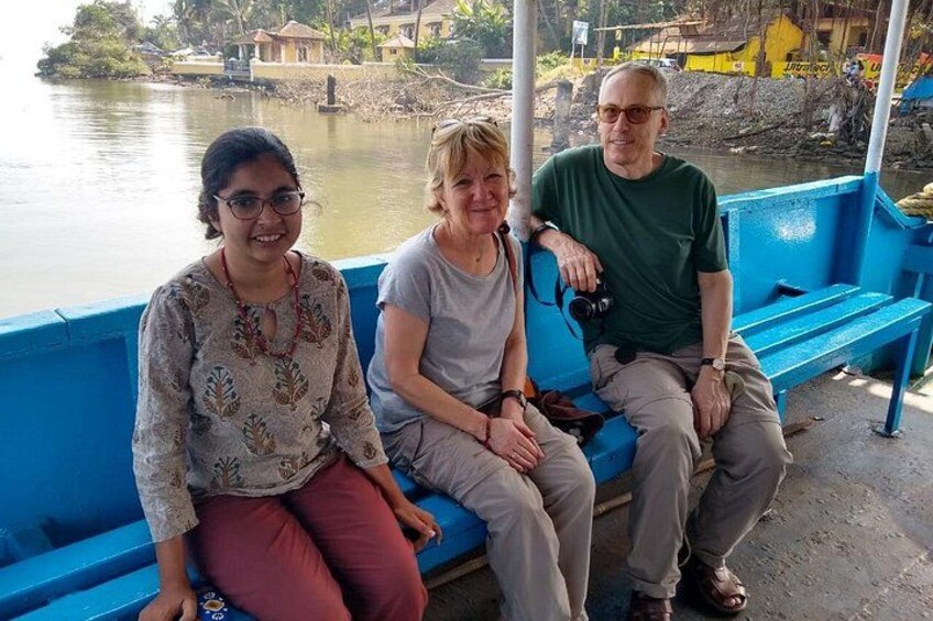 Tres personas sentadas en un banco azul junto al agua, con edificios al fondo. 3