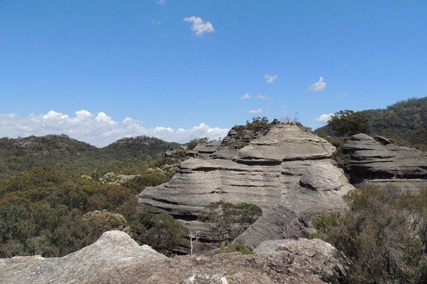 A large rock formation with layered strata, surrounded by a forested landscape. 2