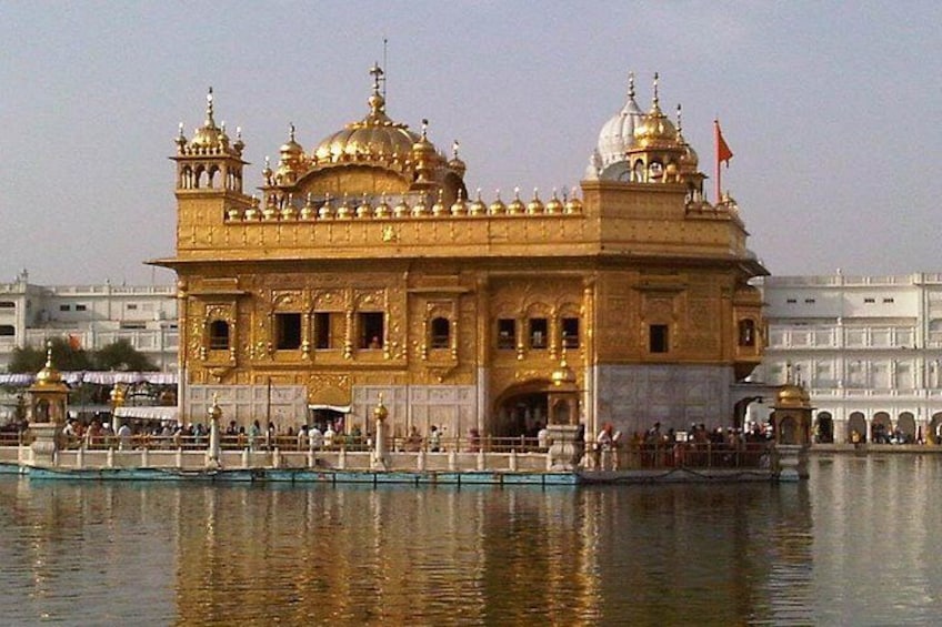Der Goldene Tempel mit Spiegelung im Wasser, umgeben von einer Brücke und weiteren Gebäuden. 1