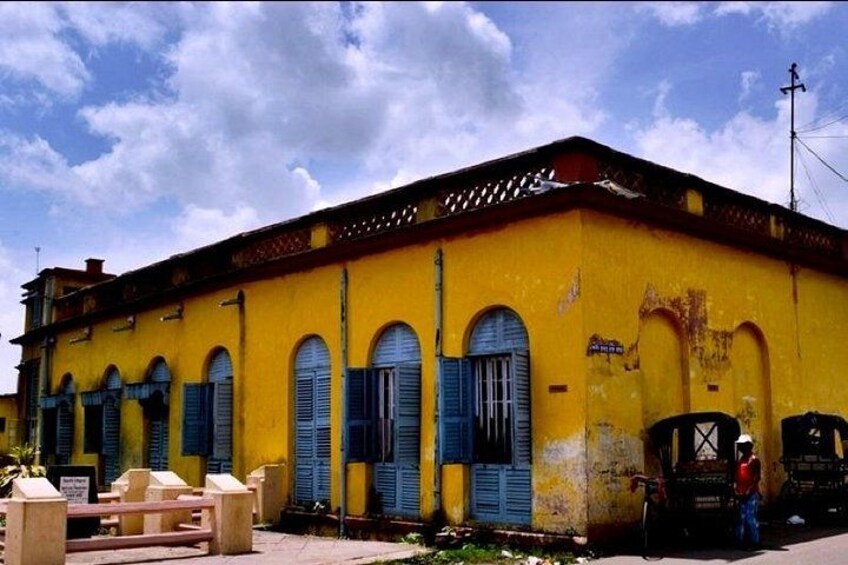 A yellow building with blue shutters and a person standing next to a bicycle. 4