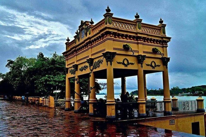 A yellow pavilion with ornate carvings, surrounded by a water body and a fence. 2