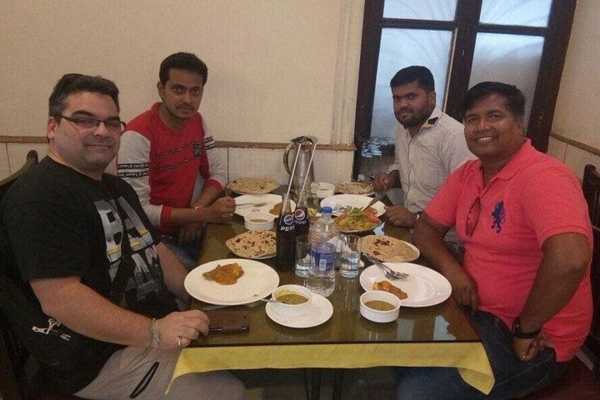 Cuatro personas sentadas alrededor de una mesa con platos de comida, botellas y una jarrón de vidrio. 2