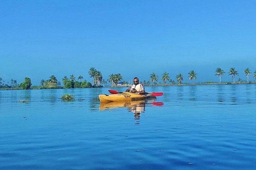 A person kayaking on calm blue water with palm trees in the background. 1