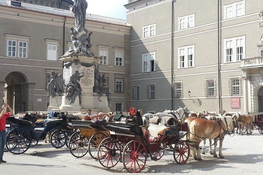 Eine Straße mit Kutschen, einer Statue und einem Gebäude mit Rundbogenfenstern. 5