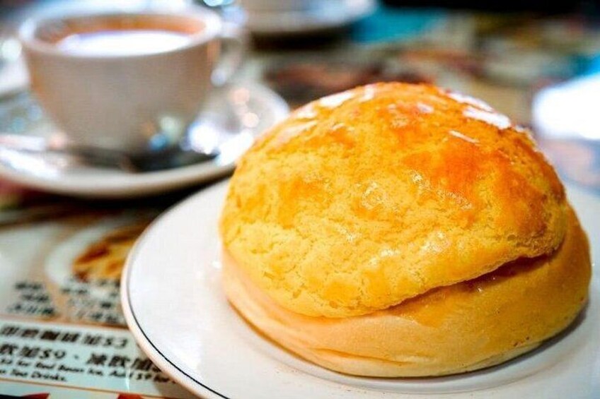 A golden-brown baked good on a white plate with a cup of a light-colored beverage in the background. 2