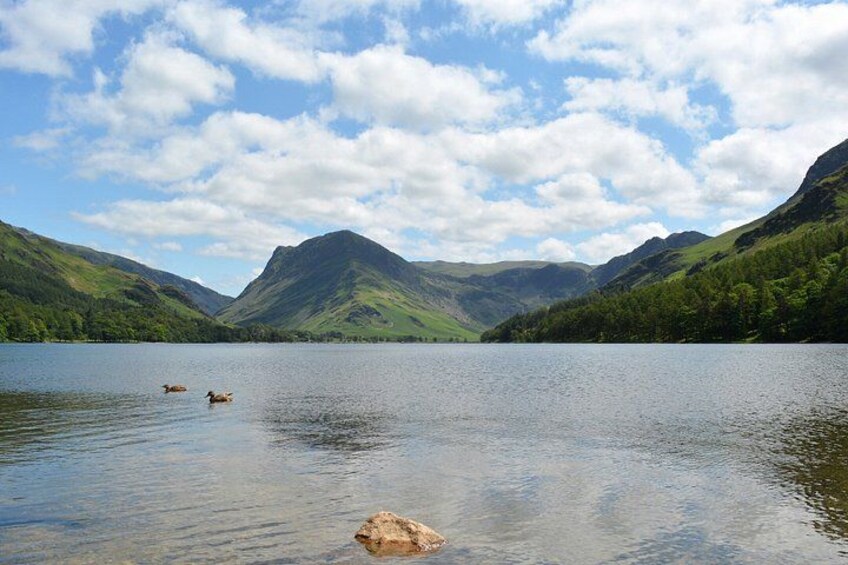 A lake surrounded by green hills and mountains under a partly cloudy sky. 2