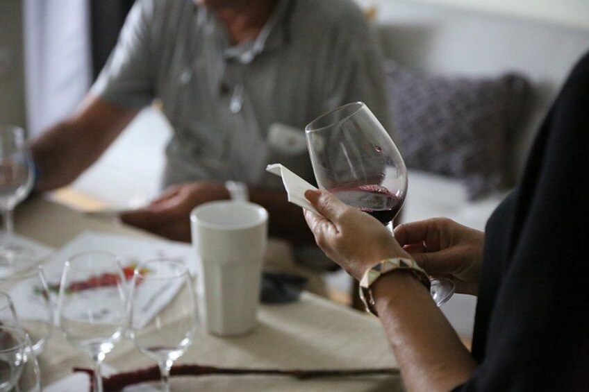 A person holding a wine glass with a napkin, a white cup, and a glass of red wine on a table. 5