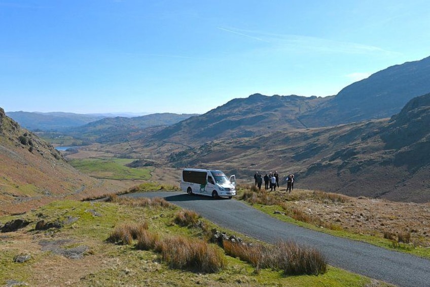 A white van on a winding mountain road with a group of people standing nearby. 3