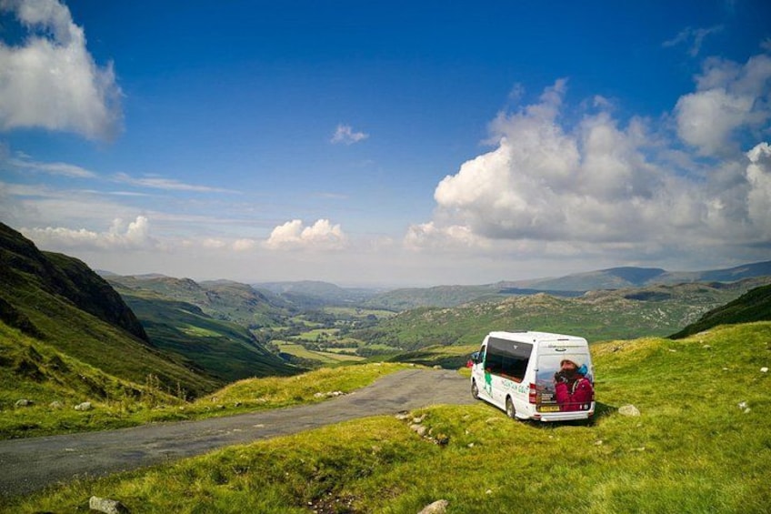 A white van parked on a grassy hillside with a scenic view of rolling hills and a clear sky. 1