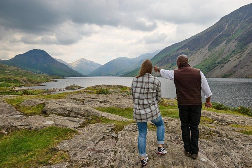 A couple walking on a rocky shore with a lake and mountains in the background. 2