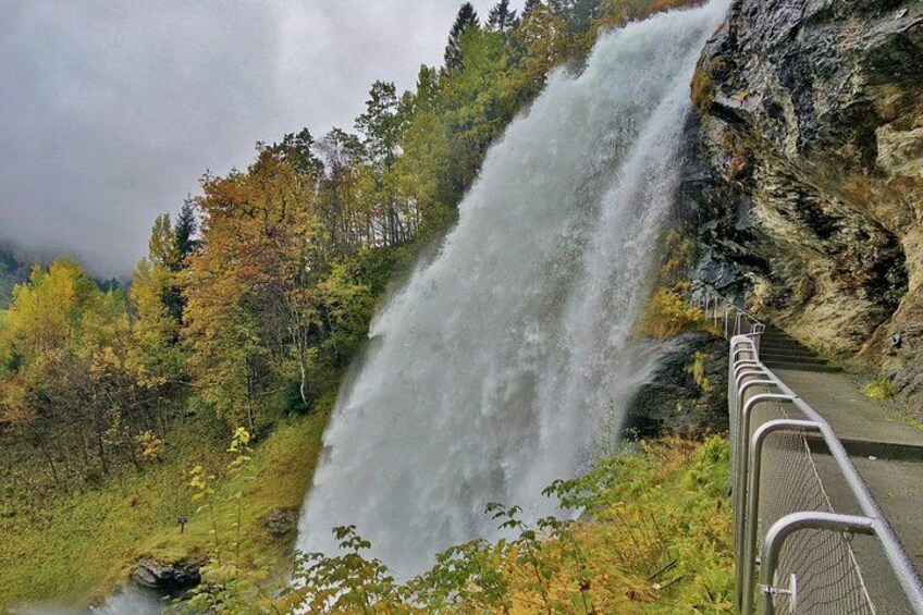 A waterfall cascading down a rocky cliff, surrounded by autumn foliage and a metal railing along the viewing path. 3