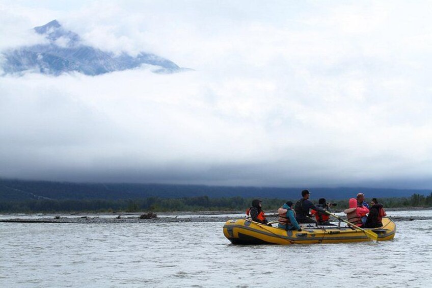 A group of people in a yellow inflatable raft on a body of water with a mountain in the background. 3