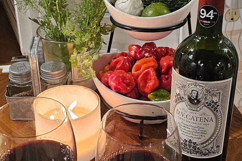 A bottle of D.V.Catena wine, a candle, glasses, a bowl of tomatoes, and a plant. 2