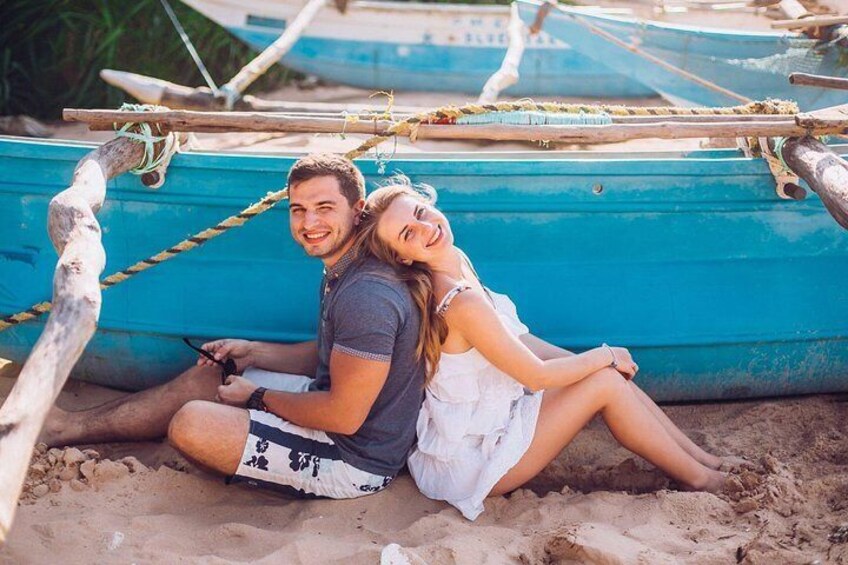 A couple sitting on the sand near a blue boat. 1