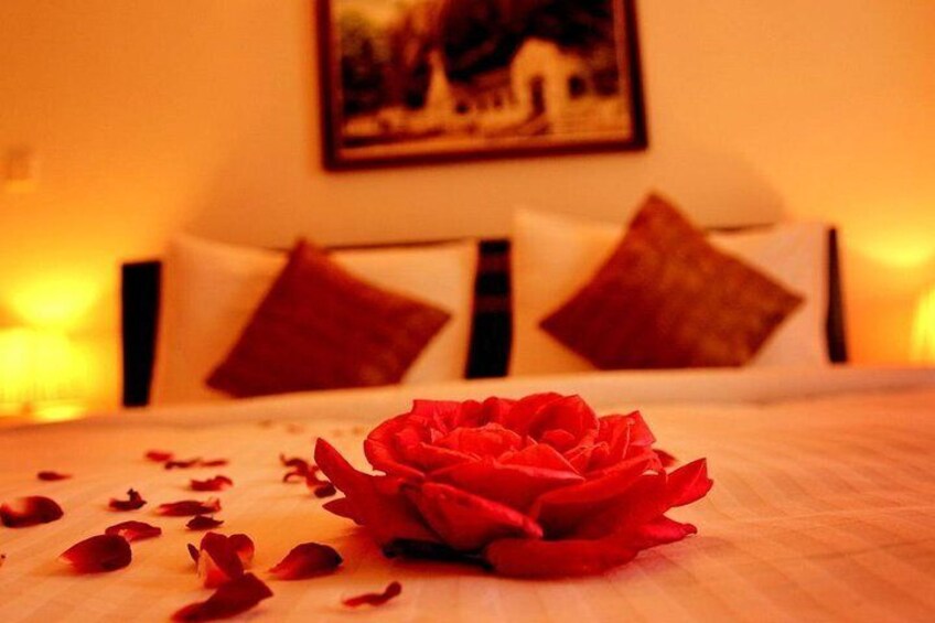 A bed with a red rose and scattered petals, a white pillow, and a painting on the wall. 4