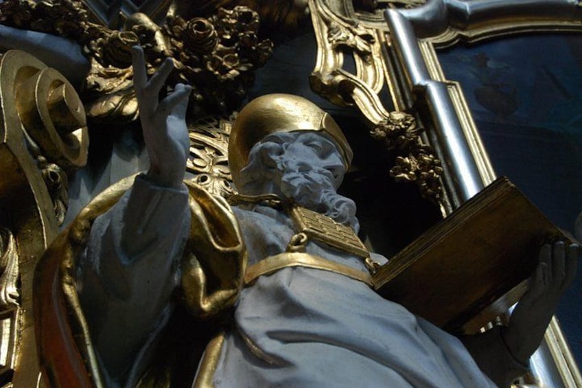 A statue of a robed figure holding a book, set against an ornate background with gold accents. 5