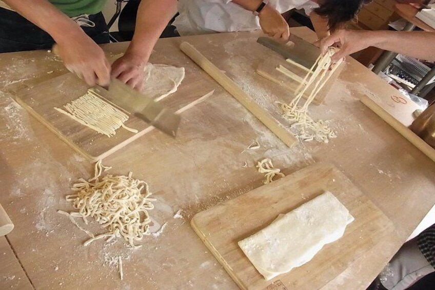 People preparing pasta on a wooden table with flour. 1