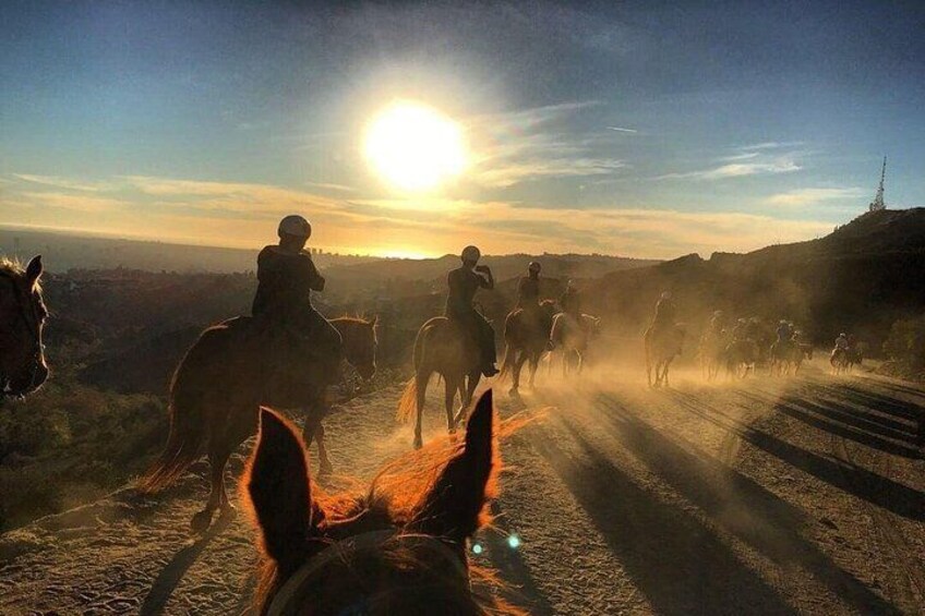 Un grupo de personas montando a caballo en un camino de tierra al atardecer. 3