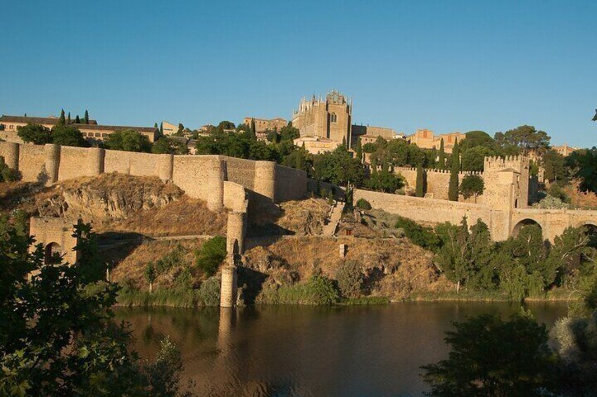 A historic stone wall and bridge over a river, with a castle in the background. 2