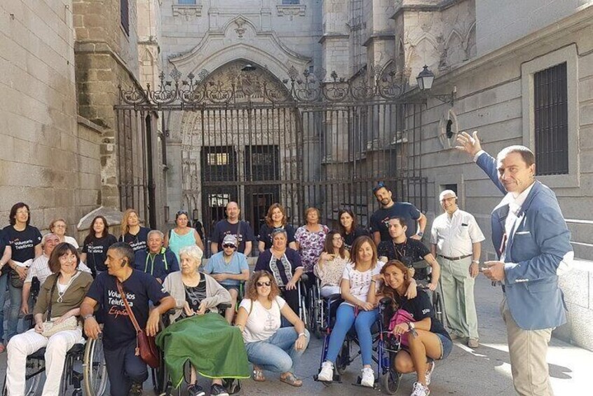 A group of people, some in wheelchairs, gathered in front of a historic building with ornate architecture. 1