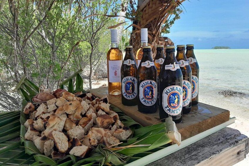 Escena de playa con una mesa que muestra botellas de cerveza Tahiti y un plato de comida. 5