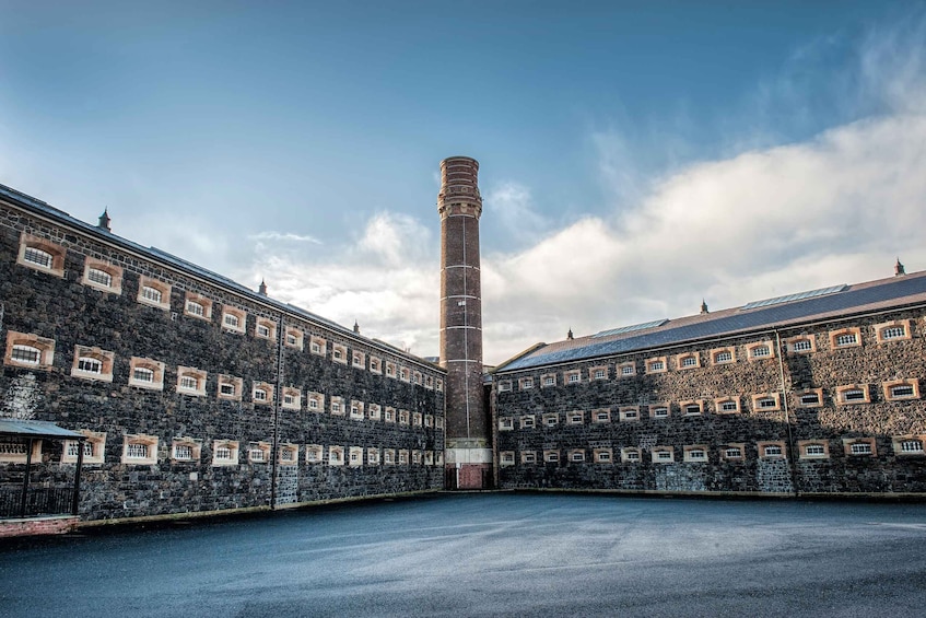 A large industrial building with a tall chimney, stone walls, and multiple windows. 1