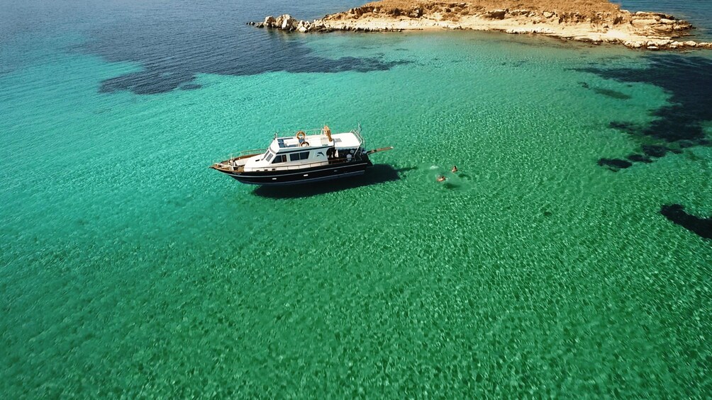 A boat on clear turquoise water with a rocky coastline in the background. 2