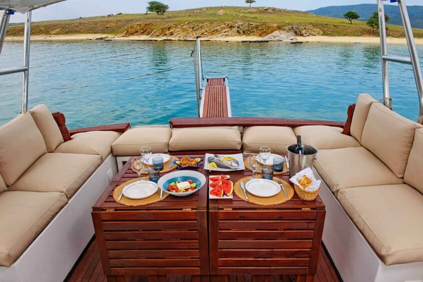 A boat deck with a table set for a meal, surrounded by a calm sea and a distant shoreline. 3