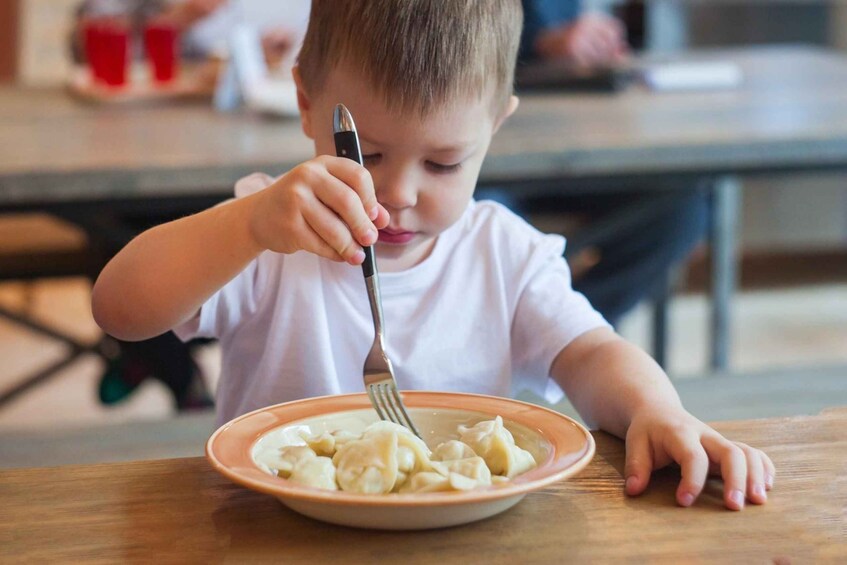 A child eating dumplings with a fork at a wooden table. 2