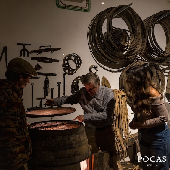 A workshop with tools and coiled materials, a person working on a barrel, and another observing. 3