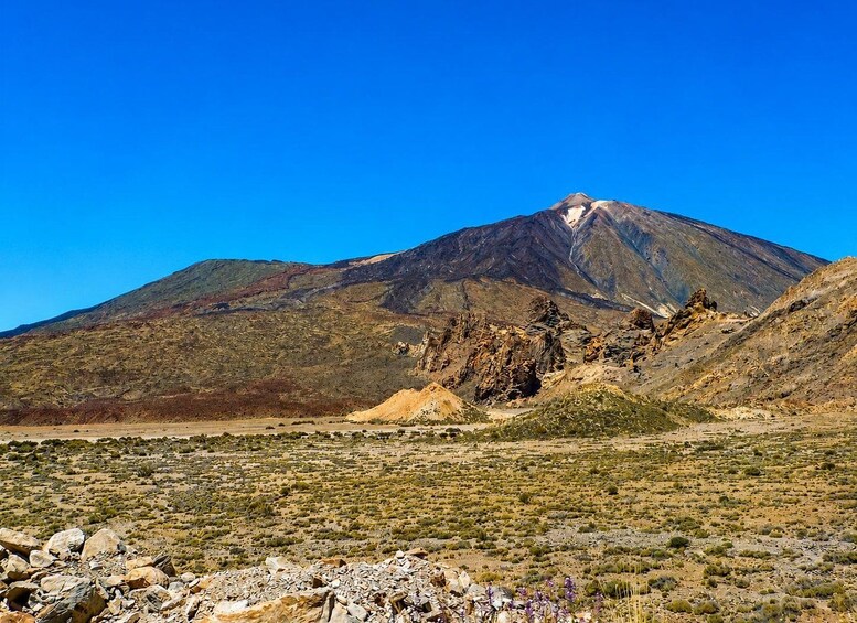 A mountain with a clear sky, rocky terrain, and sparse vegetation. 4