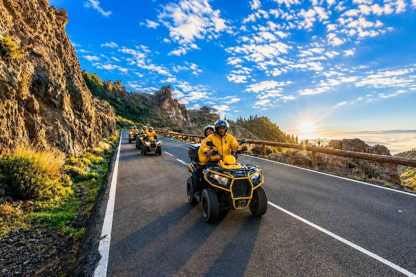 A group of people riding ATVs on a winding mountain road with rocky cliffs and a clear blue sky. 5