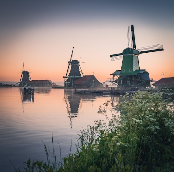 A serene sunset over a calm river with traditional windmills and houses reflecting on the water. 3