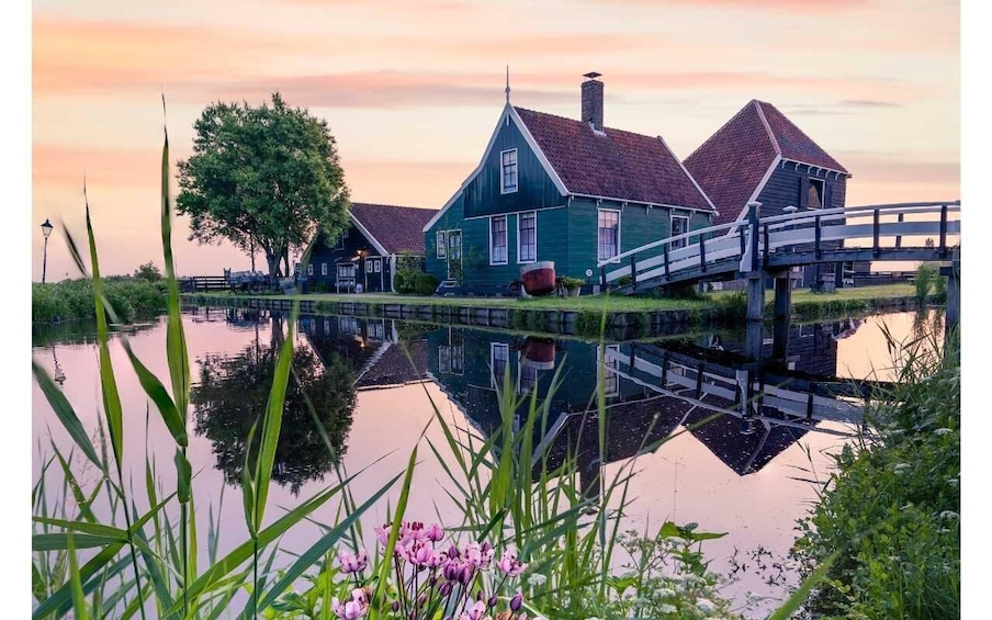 A house by a calm water body with a wooden bridge, surrounded by greenery and a tree. 4