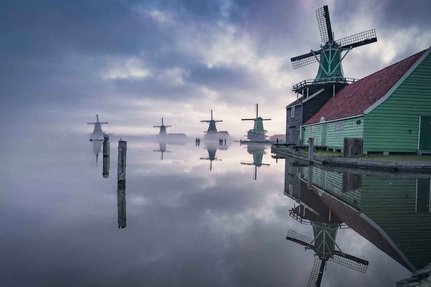 A calm water body reflecting windmills and a green building with a red roof. 2