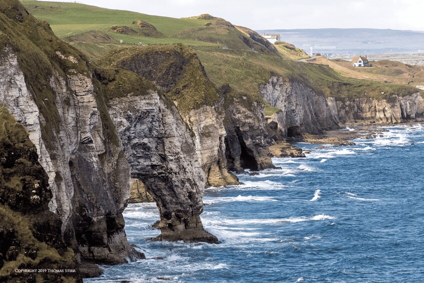A coastal landscape with prominent rock formations, a lighthouse, and a white building on a hill. 2