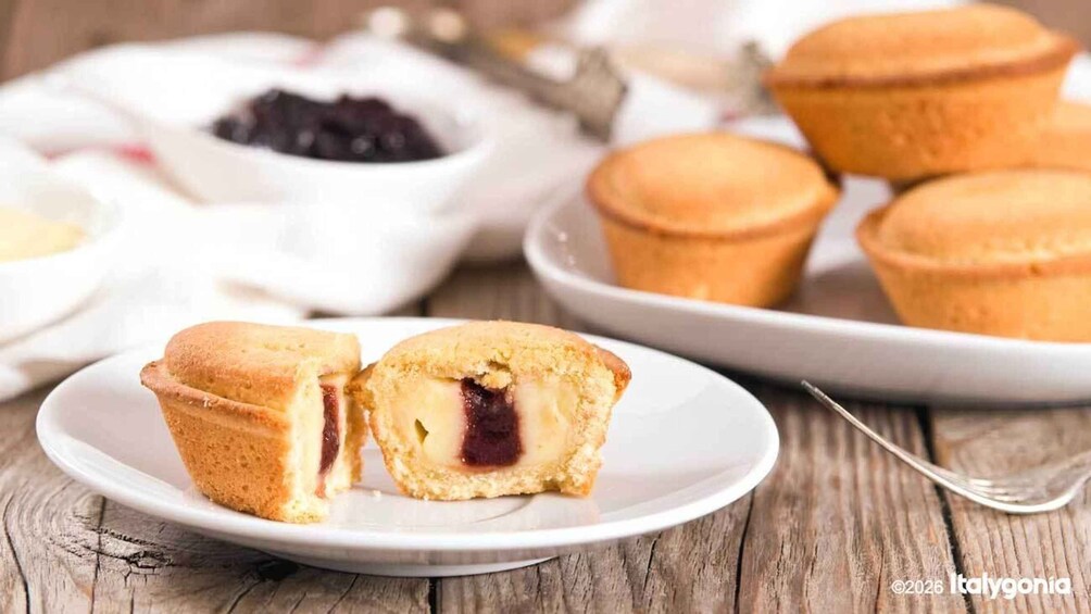 Puoliksi leikattu muffinssi, jonka täytteenä on hilloa, valkoisella lautasella. 1