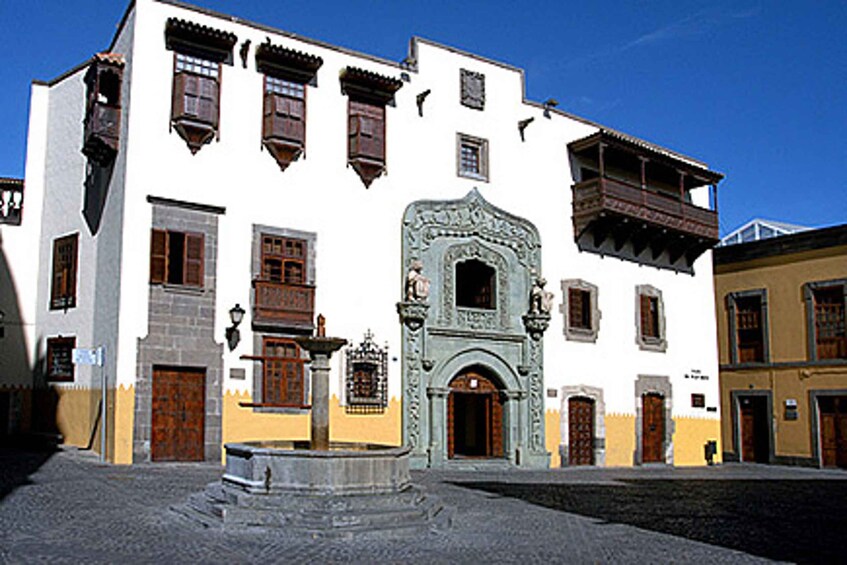 A historic street with cobblestone pavement, a fountain, and traditional buildings with ornate doors and windows. 1
