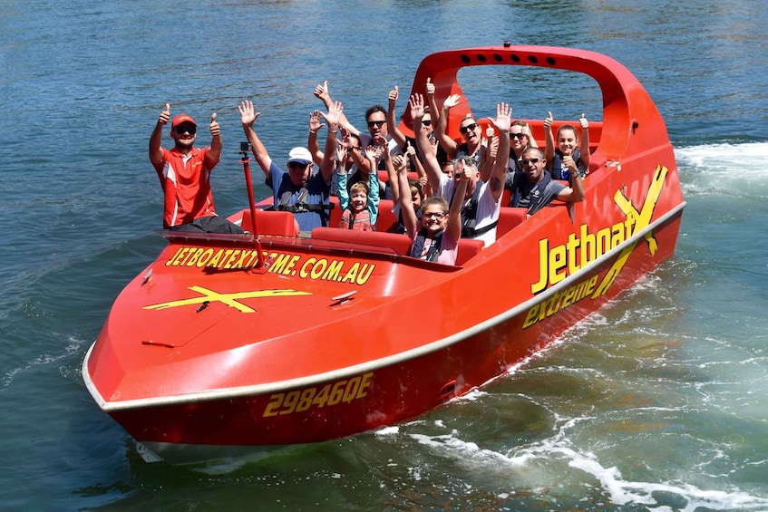 Een rode boot met mensen aan boord, die hun handen omhoog steken en duimen omhoog geven. 1