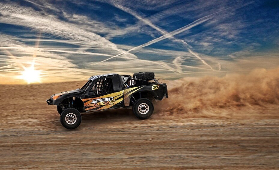 A remote-controlled car with 'SPEED VEGAS' and number 10 on it, driving on a dirt track with a sunset in the background. 1