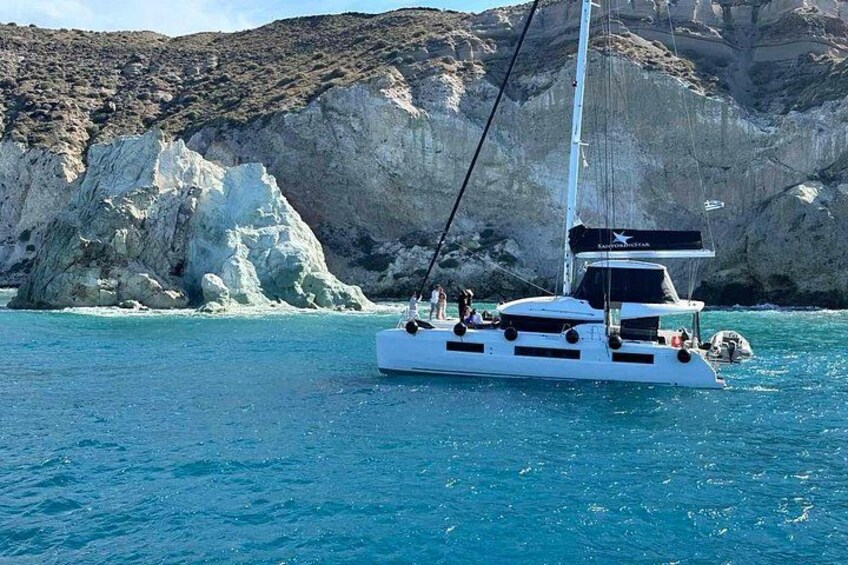 A white sailboat with passengers on a turquoise sea, with rocky cliffs in the background. 2