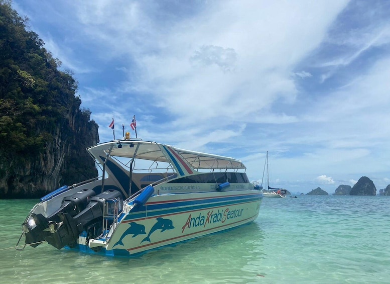 A boat named 'Anda Krabi Seautour' with dolphins on its side, docked near a rocky cliff and clear turquoise water. 1