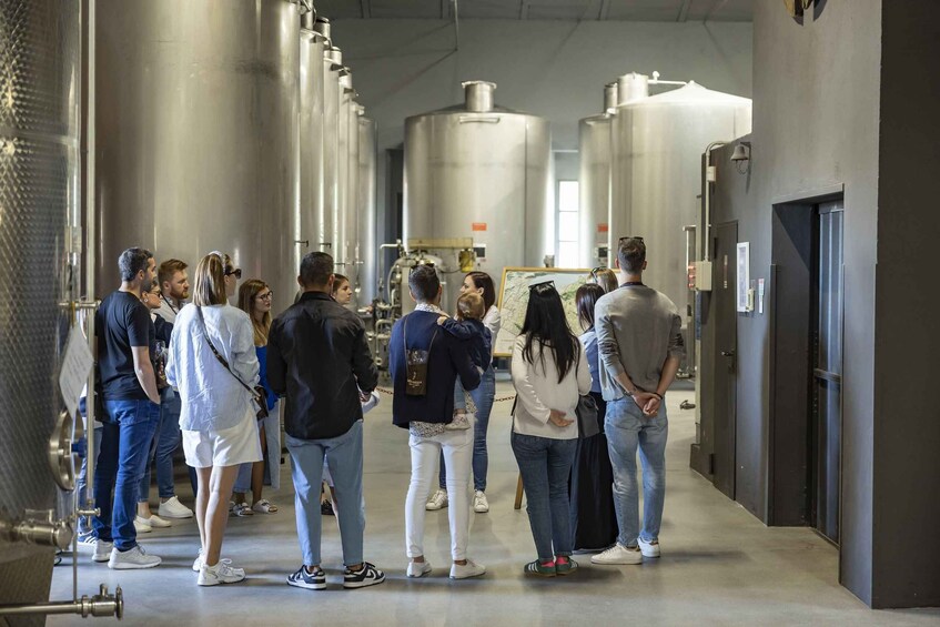 A group of people in a facility with large cylindrical tanks and pipes. 4