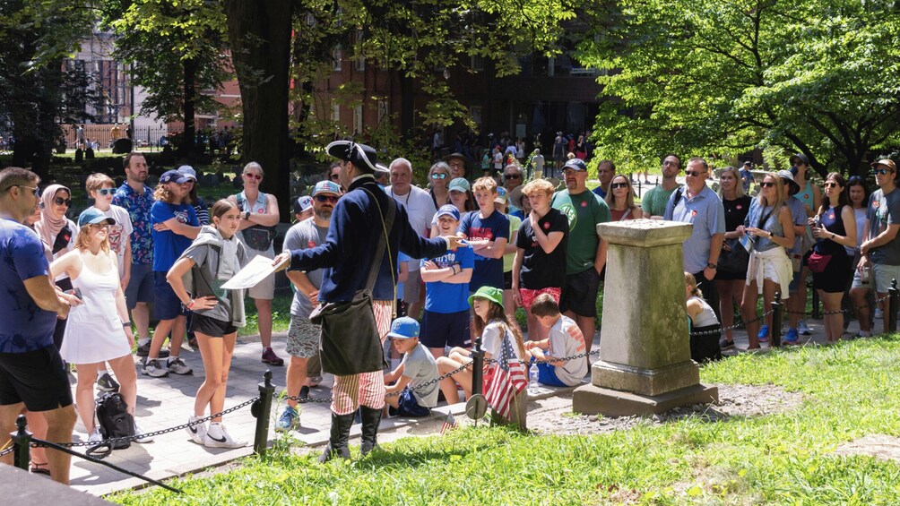 A crowd gathered around a monument in a park with trees and buildings in the background. 5