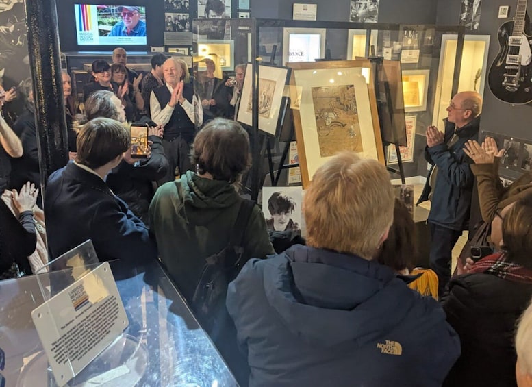 A group of people at an art exhibition, some clapping, with framed artworks on display. 5