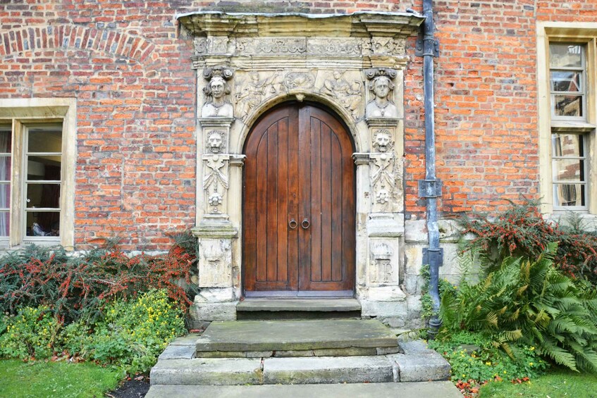 A brick building with a large wooden door, stone carvings, and a garden with various plants. 4