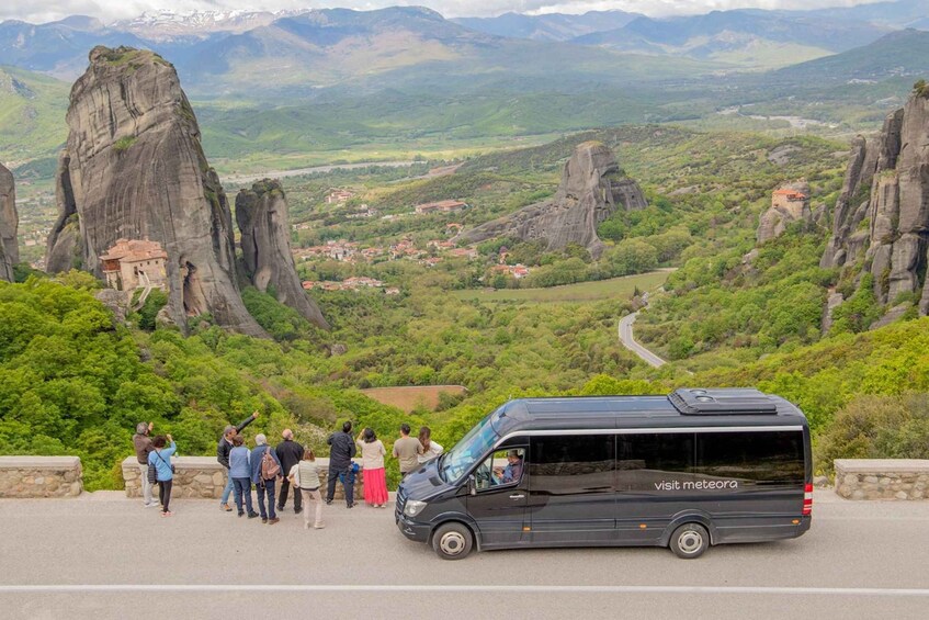 A group of people standing on a viewing platform, overlooking a valley with distinctive rock formations and a winding road. 3