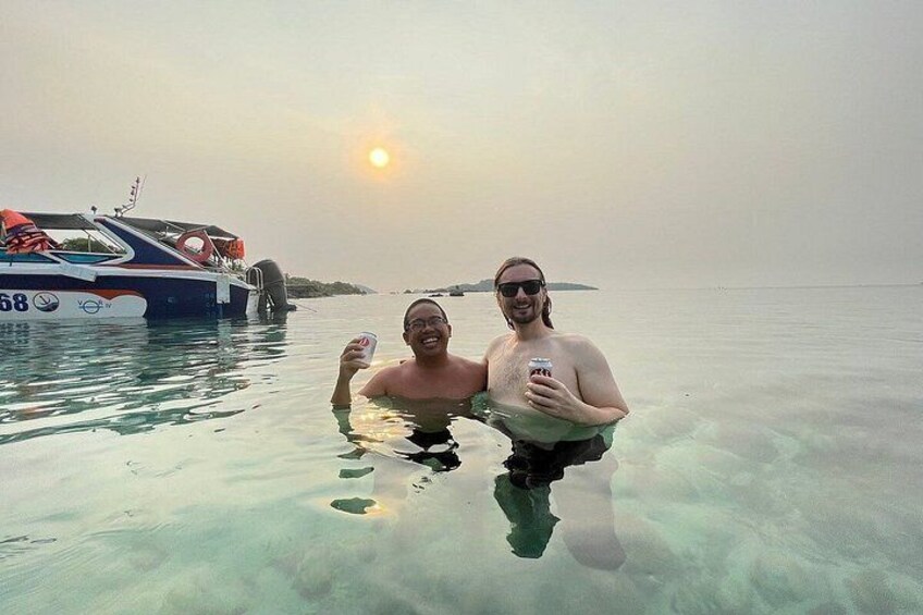 Two people in clear water, a boat with the number 68, and a sunset in the background. 2