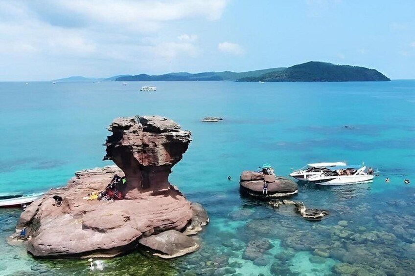 A rocky formation, clear turquoise water, boats, and a distant island. 3